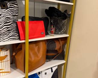 Assorted handbags and accessories including a zebra-print tote, silver textured handbag, red Mossimo clutch, tan leather shoulder bag, brown leather handbag, white and blue tote bag, glass bowl with black scarves, decorative rooster figurine, and a pair of black dress shoes.