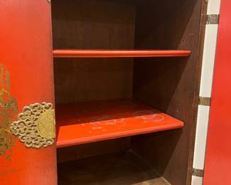 Vintage Asian-inspired red lacquer cabinet with brass decorative hardware and interior shelving.