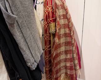 Mixed clothing rack featuring sweaters, dresses, scarves, and patterned garments on assorted hangers.