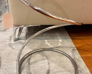 A modern chrome cantilever side table with a circular glass top and continuous tubular steel base, in the style of designs by Ludwig Mies van der Rohe and Marcel Breuer, circa 1970s–1990s.