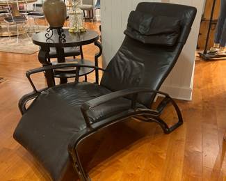 Black Leather Chaise Lounge – Modern black leather reclining chaise lounge chair with curved metal frame and head cushion, minimalist contemporary design.