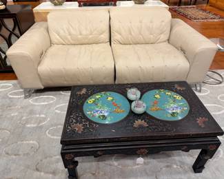 20th-century Chinoiserie coffee table with its distinctive turquoise cloisonné medallions is showcased alongside a contemporary glam-style white leather tufted sofa and a vintage Chinese-inspired black lacquer console adorned with polished circular brass hardware.