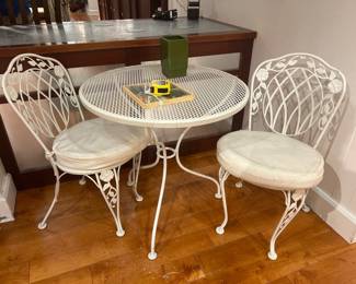 Vintage white wrought iron patio bistro set with round mesh table and two matching chairs.