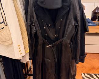 Black belted leather coat with shearling-style collar displayed on clothing rack with coordinating black handbag.