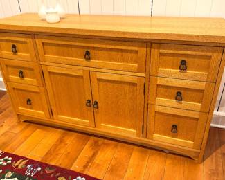 A solid oak sideboard with paneled cabinet doors and multiple drawers featuring ring pulls, in an Arts and Crafts / Mission-style design, likely circa 1990s–2000s, influenced by the work of Gustav Stickley.
