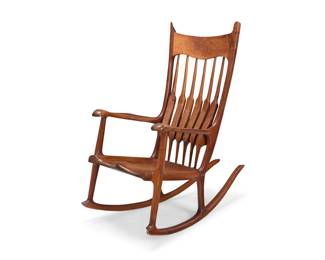 28 Charles Jacobs (1930-2007) A California Studio Craft rocking chair, 1986 Incised signature and date to seat underside: Charles Jacobs / 7-14-86; With label: handcarved heirloom furniture by Charles Jacobs / claremont, california In the style of Sam Maloof (1916-2009), with spindle back, flared armrests, and shaped seat, raised on rockers 46.25" H x 26.5" W x 44" D Estimate: $1,000 - $2,000