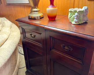Antique dark wood side cabinet with brass lamp, red vase, and figurines