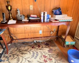 Wooden console table with brass lamp, books, and oriental area rug
