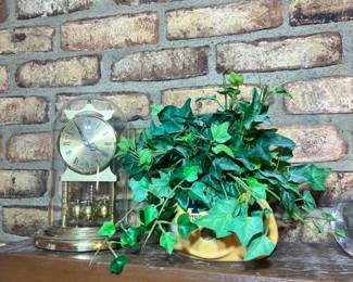 A classic brass anniversary clock under a glass dome, paired with an artificial ivy-filled Notre Dame football planter