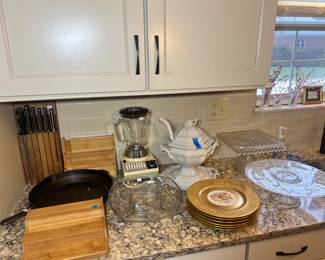 Vintage Osterizer blender, a large white ironstone tureen with ladle, crystal cake stands, a cast-iron skillet, and gold-rimmed floral plates