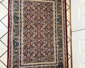 Detailed rug featuring a traditional navy and cream border with a dense red floral field