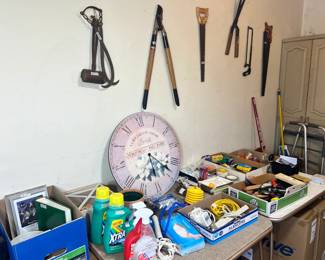 Garden Tools & Home Goods – Large wall clock, heavy-duty loppers, hand saws, and assorted household cleaning supplies and hardware