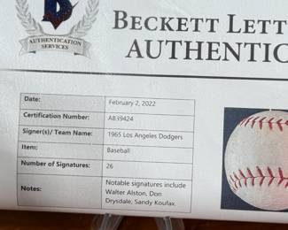 This lot features a baseball with twenty-six (26) autographs from the 1965 Los Angeles Dodgers. Notable signatures include Walter Alston, Don Drysdale, and Sandy Koufax. Accompanied in a display case with authentication papers from Beckett.