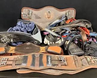 Collegiate & Professional Choice Horse Tack Collection Featuring Girths, Stirrups, Gloves & More. This grouping includes a useful assortment of horse tack and riding accessories suitable for everyday riding, training, or barn use. The collection features several girths including a Collegiate girth and additional shaped girths, designed to help secure the saddle comfortably while allowing freedom of movement for the horse. Also included are black stirrups marked “Compositi,” a lightweight composite stirrup known for durability and stability in the saddle, along with additional tack components commonly used for English riding setups.