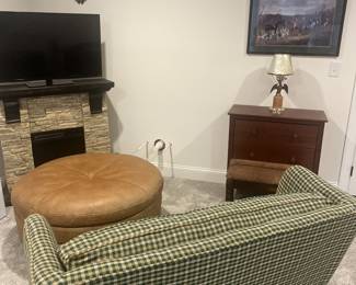 Electric fireplace, mounts ,oversized round leather ottoman, plaid printed loveseat, wooden end table, brass eagle lamp.