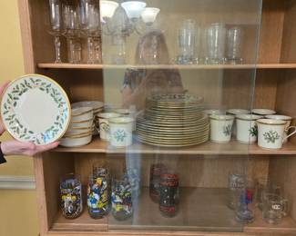 Light wood cabinet with glass door hutch. Lenox Christmas Holly, Etched glasses, collector glasses Smurf, Miss Piggy...