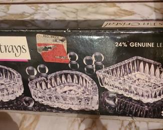 A boxed set of three crystal ashtrays made from 24% lead crystal, each with cut‑glass patterns that create strong sparkle and reflection. The packaging shows three different designs, all with faceted edges and decorative cuts typical of mid‑century or vintage crystal gift sets. These sets were often sold as barware or decorative tabletop pieces and are now collected for their weight, clarity, and retro appeal.  Priced at $25