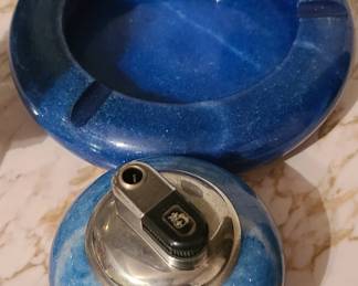 A coordinated mid‑century blue marble ashtray and table lighter set, made from ceramic or resin with a glossy swirl pattern in shades of blue and white. The ashtray features three cigarette rests, and the matching lighter has a chrome‑tone top with a classic push‑down ignition mechanism. The set has a stylish retro look—very 1960s–1970s—and works well as décor even for non‑smokers because of its color, weight, and sculptural presence.  Priced at $75 for the set