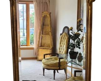 A tall, ornate vintage gold wall mirror with an elaborate frame featuring scrolling curves and floral detailing at both the top and bottom. The gold finish has a warm, aged patina that enhances its antique character. Its generous size and decorative silhouette make it a striking focal point for an entryway, living room, or bedroom, especially in homes styled with traditional, Victorian, Hollywood Regency, or French‑inspired décor.  Priced at $75