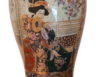 A decorative hand‑painted Japanese‑style ceramic vase featuring an elegant figure in traditional attire surrounded by richly detailed floral patterns and gold embellishment. The artwork includes vibrant colors—reds, greens, blues, and pinks—layered with raised and gilded accents that give the piece depth and texture. The upper and lower sections are finished with ornate swirling motifs, and the vase sits on a dark wooden stand that enhances its display presence. The style resembles Satsuma‑inspired or Kutani‑influenced decorative export pieces, known for their intricate designs and heavy use of gold.  Priced at $40