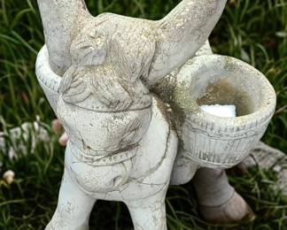 A small vintage concrete donkey planter, designed as a donkey carrying two side baskets. The piece shows weathered aging, with natural cracks and patina that give it rustic charm. Its worn surface and outdoor discoloration suggest it has been a long‑loved garden ornament. The baskets can hold small plants, succulents, or decorative stones, making it both functional and decorative. It fits well with cottage‑garden, farmhouse, or vintage outdoor décor.  Priced at $30