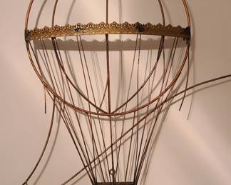 Vintage Curtis Jere hot air balloon, crafted from thin, curved metal rods that form the outline of the balloon’s envelope. A gold accent band wraps around the widest part, adding contrast and a touch of elegance. The basket is also metal and includes two stylized human figures, giving the piece personality and movement. The open‑frame design casts soft shadows on the wall, making it visually interesting and dimensional without feeling heavy. This style fits well with modern, industrial, eclectic, or travel‑themed décor.  