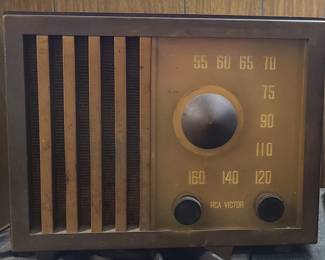 A vintage RCA Victor tabletop radio with a classic mid‑century design. The cabinet has a warm wood tone with vertical slats over the speaker on the left, and on the right a rectangular tuning dial marked from 55 to 160 (AM band). Two black knobs sit below the dial for tuning and volume, with the RCA Victor nameplate beneath them. Its compact size and iconic styling make it a collectible display piece, especially for those who enjoy early radio history or mid‑20th‑century electronics.  Priced at $75