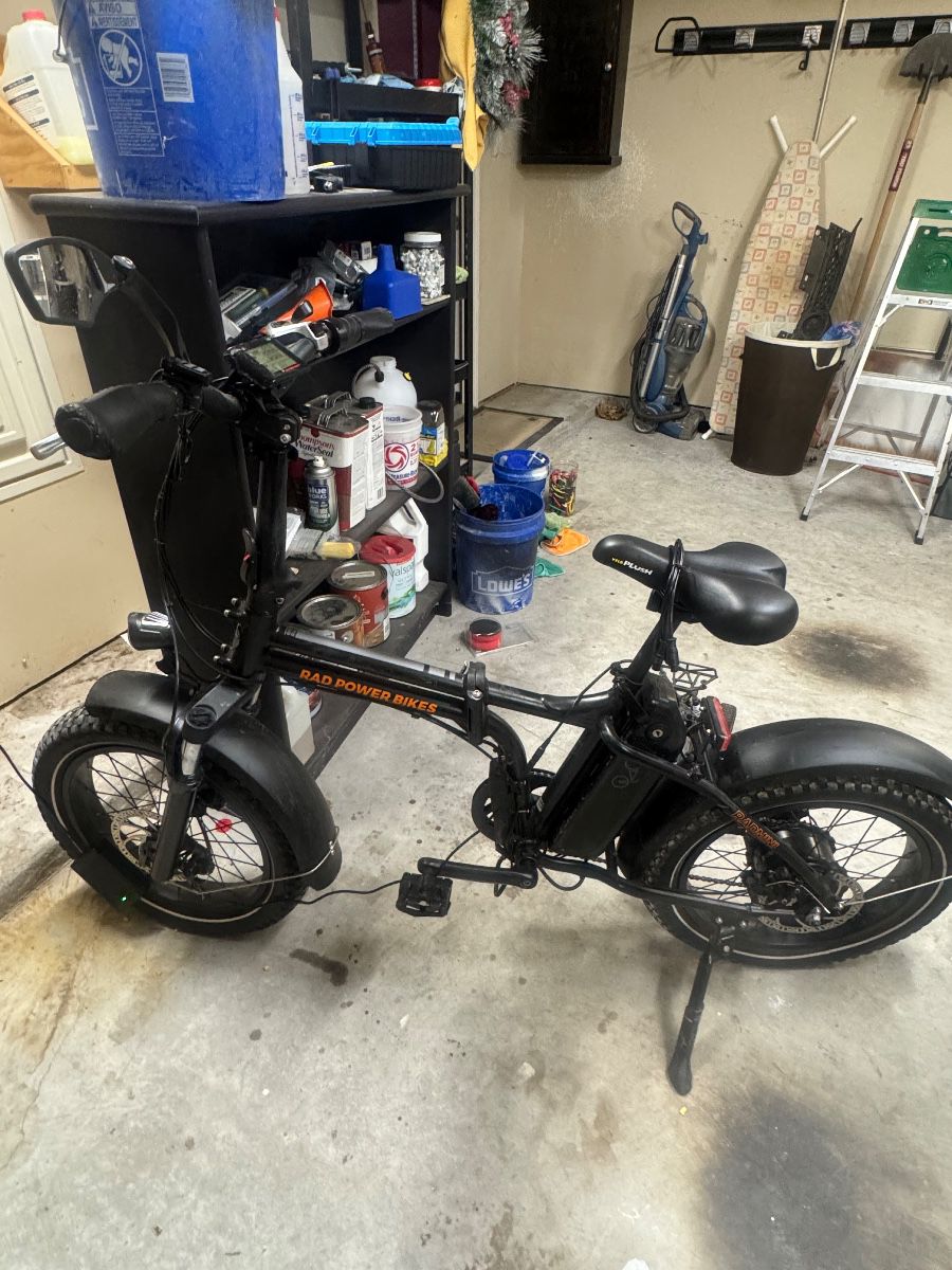 Black moped-style scooter with pedals and seat, photographed in a garage.