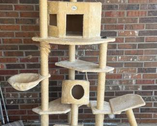 Tall beige cat tree with multiple platforms, scratching posts, and an enclosed cubby, set against a brick wall.