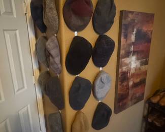 Wall with multiple hats hung on hooks alongside decorative artwork.