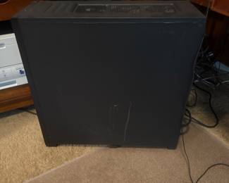 Black desktop computer tower placed on the floor next to a desk, with cables visible.