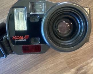 Film camera with detachable zoom lens and flash unit, placed on a wooden floor.