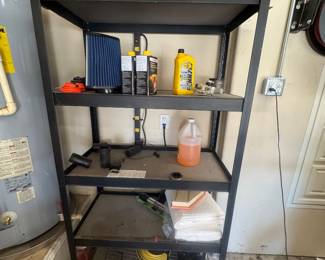 Black metal shelving unit in a garage holding cleaning supplies, a small cooler, and various household items.