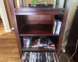 Wooden shelving unit containing multiple rows of DVDs with a green potted plant on top.