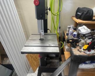 Benchtop band saw with metal table and vertical blade in a garage workshop.