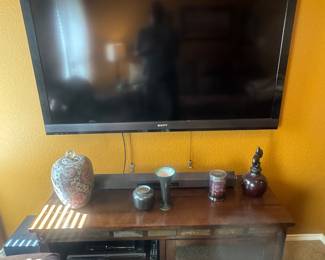 Flat-screen TV mounted on a wall above a wooden media console with glass doors and decorative items.