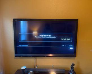 Wall-mounted flat-screen TV on yellow-gold wall with small table and decorative items below.