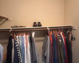 Closet with an assortment of men's shirts and jackets hanging on a clothing rack with overhead shelf.