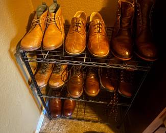 Multiple pairs of brown leather boots arranged on a metal shoe rack against a yellow wall.