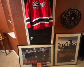 Red hockey jersey displayed on hanger along with framed Sopranos posters and a decorative wall plaque.