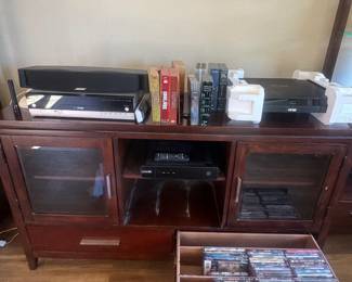 Wooden media console with glass doors, holding DVDs and electronic components.