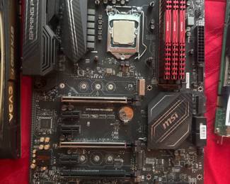 Black PC motherboard with red heat sink and multiple connectors, photographed on red cloth.