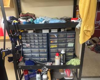 Metal shelving unit with drawers and trays filled with various tools and supplies, with a yellow towel hanging on the side.