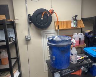 Garage workshop shelving with tools, supplies, and a large blue plastic bucket or cooler.