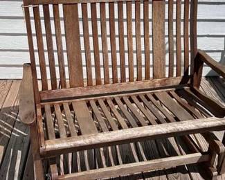 Design: This lot features a high-quality wooden outdoor glider bench with a classic slatted back and seat design. Construction: The bench is constructed from durable wood, ideal for porch or deck use. Mechanism: It features a smooth gliding base for comfortable outdoor relaxation. Condition: The piece shows some natural weathering consistent with outdoor placement, adding to its rustic appeal.