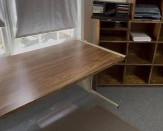 Add a touch of retro-industrial style to your office with this two-piece furniture lot featuring a wood-grain finish and clean lines. This lot includes: Sled-Base Writing Desk: A streamlined desk featuring a rich wood-grain laminate top and a modern, silver-tone metal sled-base frame. Perfect for a laptop station or a creative workspace. 12-Section Wooden Cubby Organizer: A versatile, open-front storage unit with twelve equal-sized cubbies. Ideal for sorting mail, organizing office supplies, or displaying a collection. Bonus Desktop Organizers: Includes the black tiered letter trays and specialized media/document organizers currently pictured on top of the cubby unit. Condition: Both pieces are in good, functional condition with light surface wear consistent with professional use.