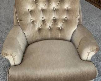 Style: This lot features a classic vintage-style swivel rocker armchair upholstered in a soft, tan/gold velvet fabric. Design: The chair includes a pleated skirt base, button-tufted accents on the interior arms, and a comfortable, high-back silhouette. Functionality: Designed with both swivel and rocking capabilities for versatile comfort. Condition: The upholstery shows light wear consistent with age, but remains in good overall condition with no major visible tears. Smoke free pet free