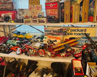 Automotive and transportation collectibles display featuring model motorcycles, die-cast cars, vintage aircraft and Texaco aviation collectibles, boats, trains, and boxed vehicle models including classic cars and roadsters. Packed shelves with display-ready transportation memorabilia for collectors, hobbyists, and resellers.