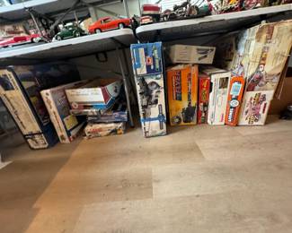 Under-table stash of vintage train sets and model railroad items, including boxed Lionel, Bachmann, and other train and hobby kits alongside die-cast vehicle displays. Great selection for train collectors, hobbyists, and resellers looking for model railroading finds.