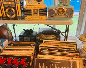 Vintage record and music display with retro tabletop radios, jukebox-style decor, record players, and boxes of vinyl albums. Great mix of nostalgic audio pieces and LP records for music collectors, decorators, and resellers.